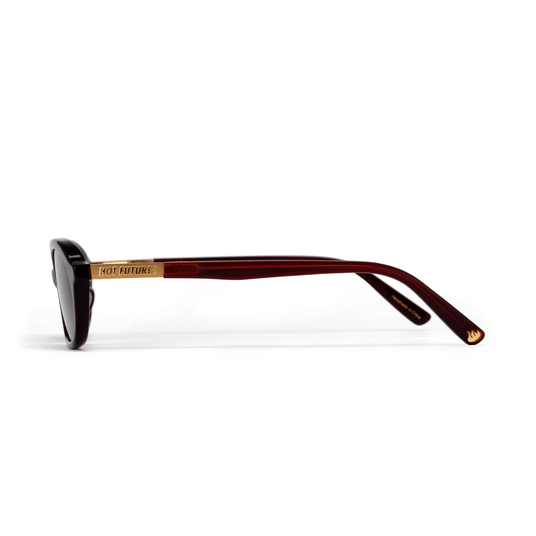Sunglasses with a gold frame and cherry red arms on a white background