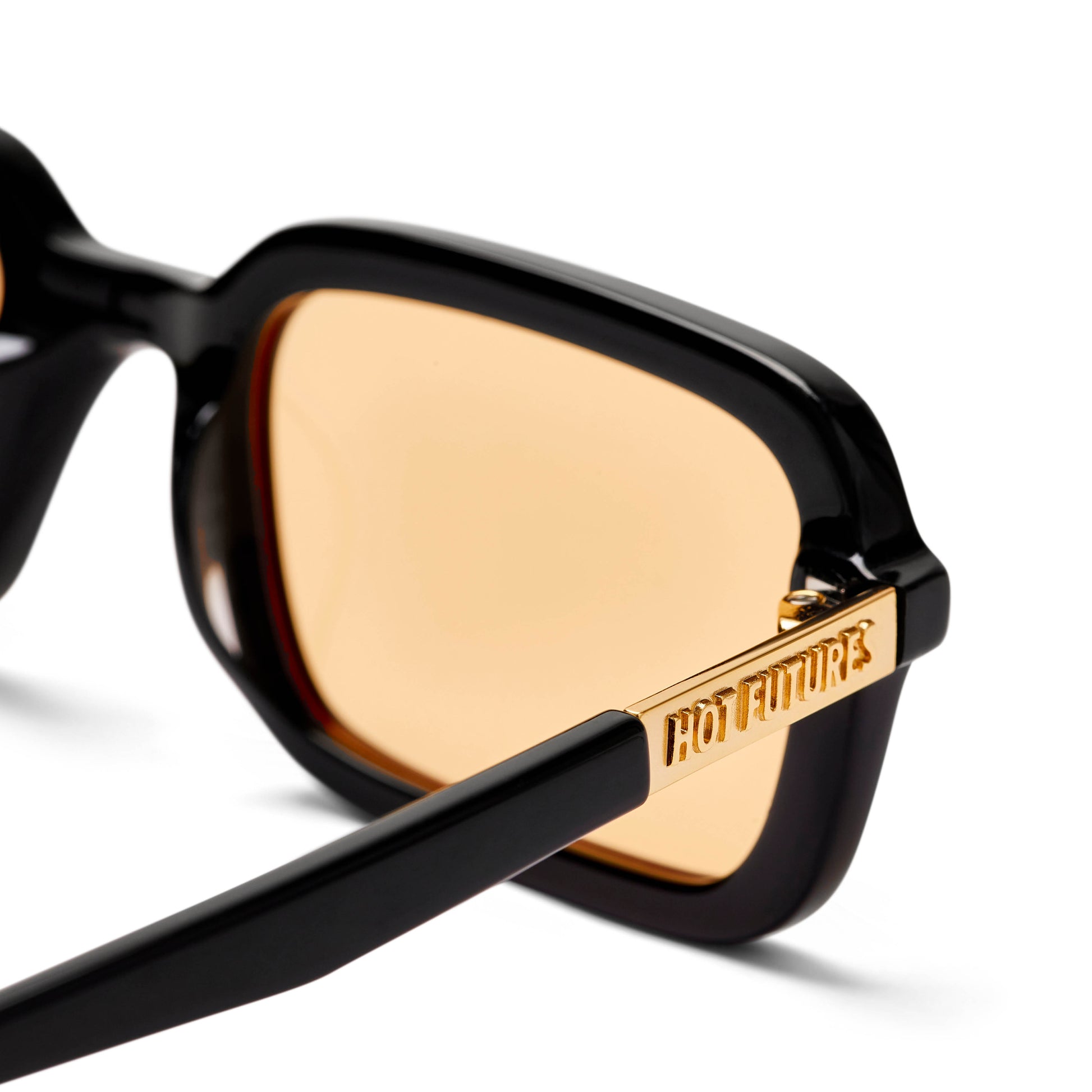 Close up shot of the Dime Sunglasses in Gloss Black frame with orange amber lenses, with the gold Hot Futures text branding on the arms