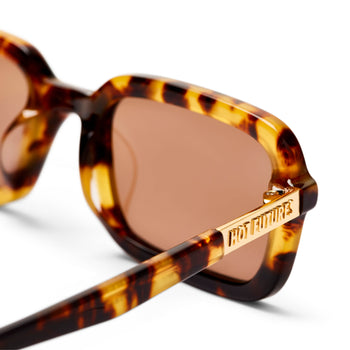 Close up shot of the Dazed tortoiseshell tan sunglassse, showing the tan lens and the gold Hot Futures text branding. 