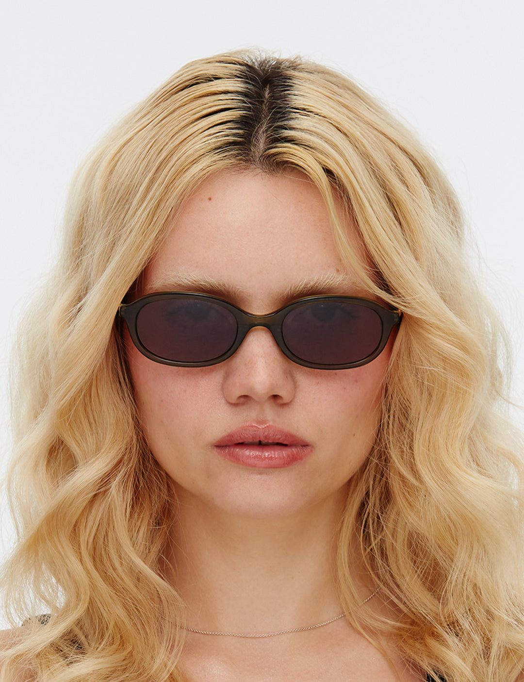 Person with blonde hair wearing dark sunglasses against a white background