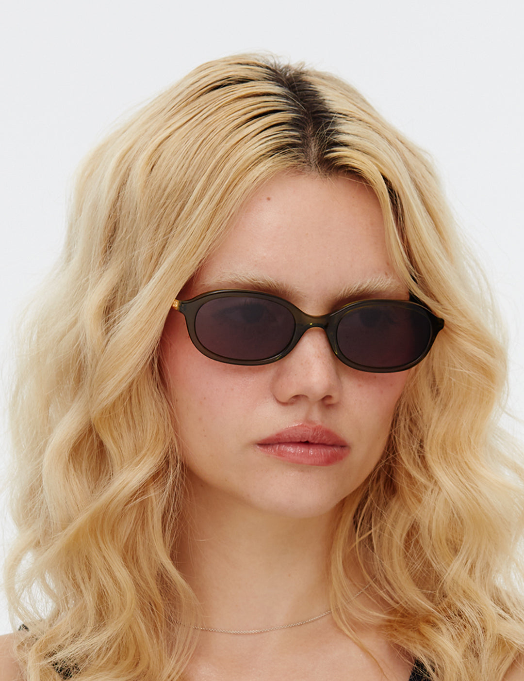 Person with wavy blonde hair wearing dark sunglasses against a white background