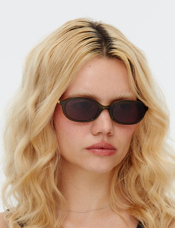 Person with wavy blonde hair wearing dark sunglasses against a white background