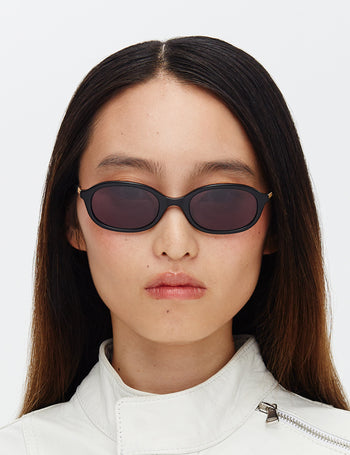 Person wearing dark sunglasses and a white jacket on a light gray background