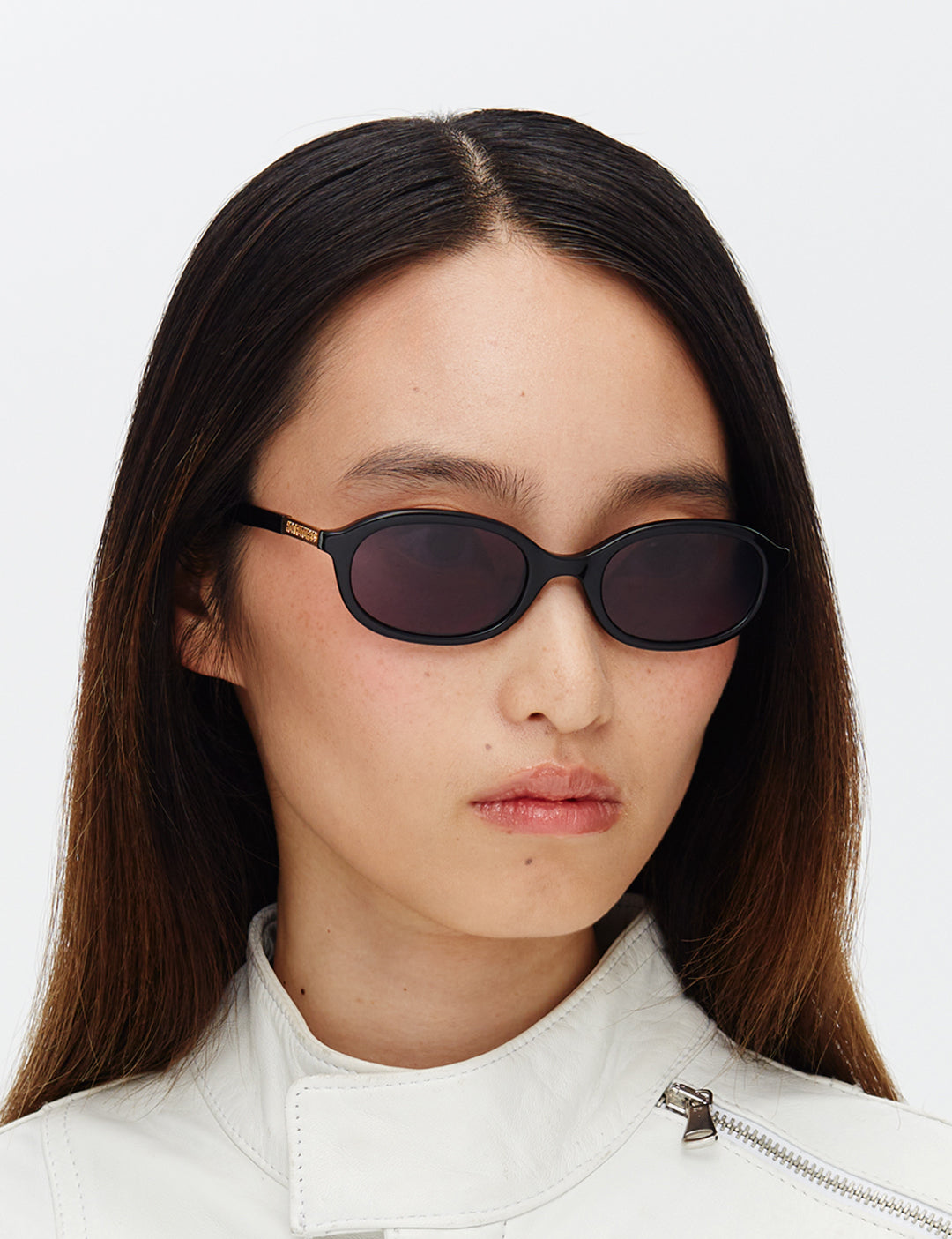 Person wearing black sunglasses and a white jacket on a light gray background