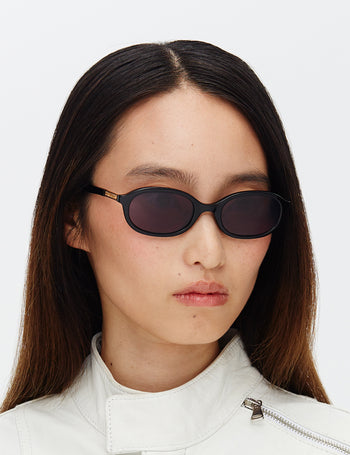 Person wearing black sunglasses and a white jacket on a light gray background