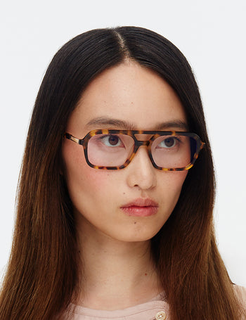 Person wearing tortoiseshell glasses against a white background
