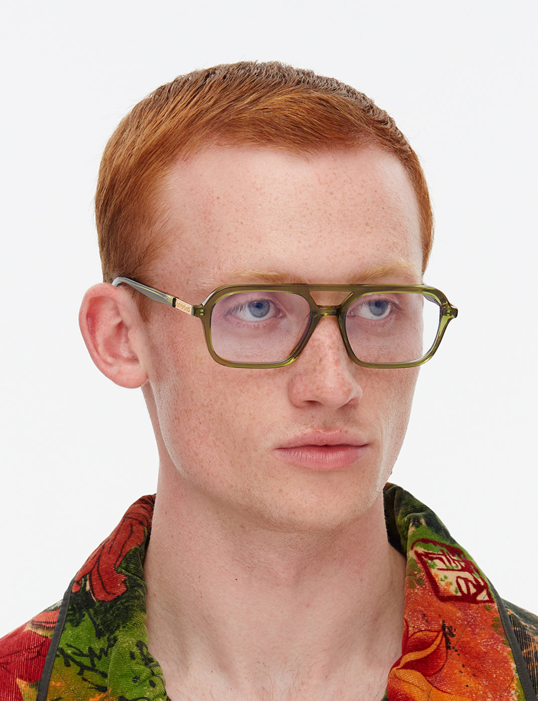 Person wearing green glasses with a colourful shirt on a white background