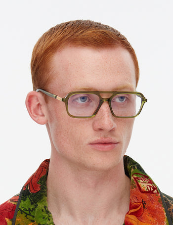 Person wearing green glasses with a colourful shirt on a white background