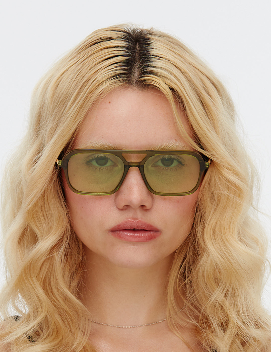 Person with blonde hair wearing green sunglasses against a white background