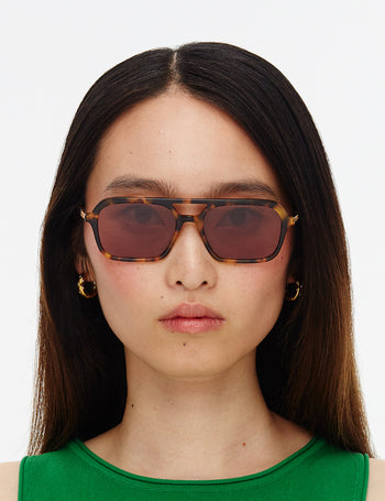Woman wearing tortoiseshell sunglasses with a plain background