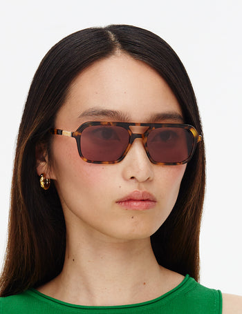 Person wearing tortoiseshell sunglasses with a plain background
