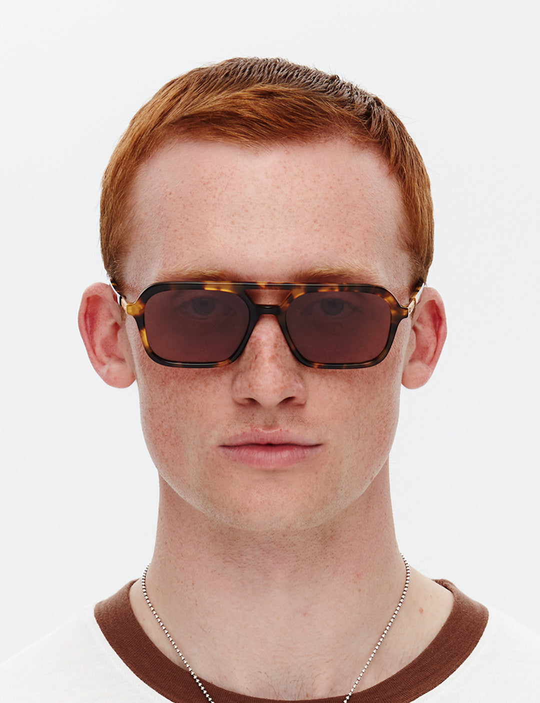 Model wearing a pair of tortoiseshell patterned sunglasses with a slim rectangular aviator frame 