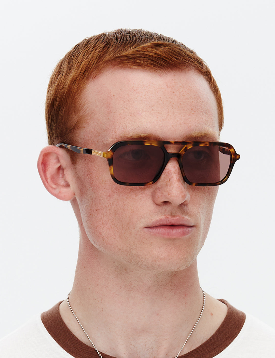 Person wearing tortoiseshell sunglasses with a plain background