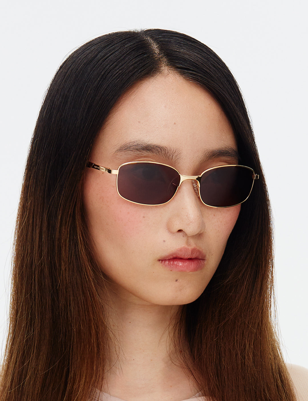 Person wearing gold-framed sunglasses with a plain background