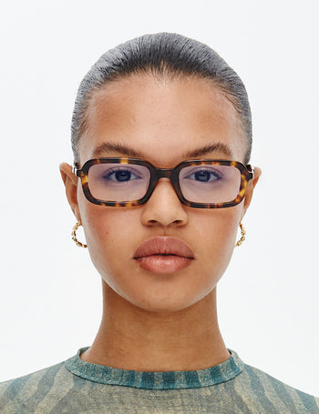 Person wearing tortoiseshell glasses with a neutral background