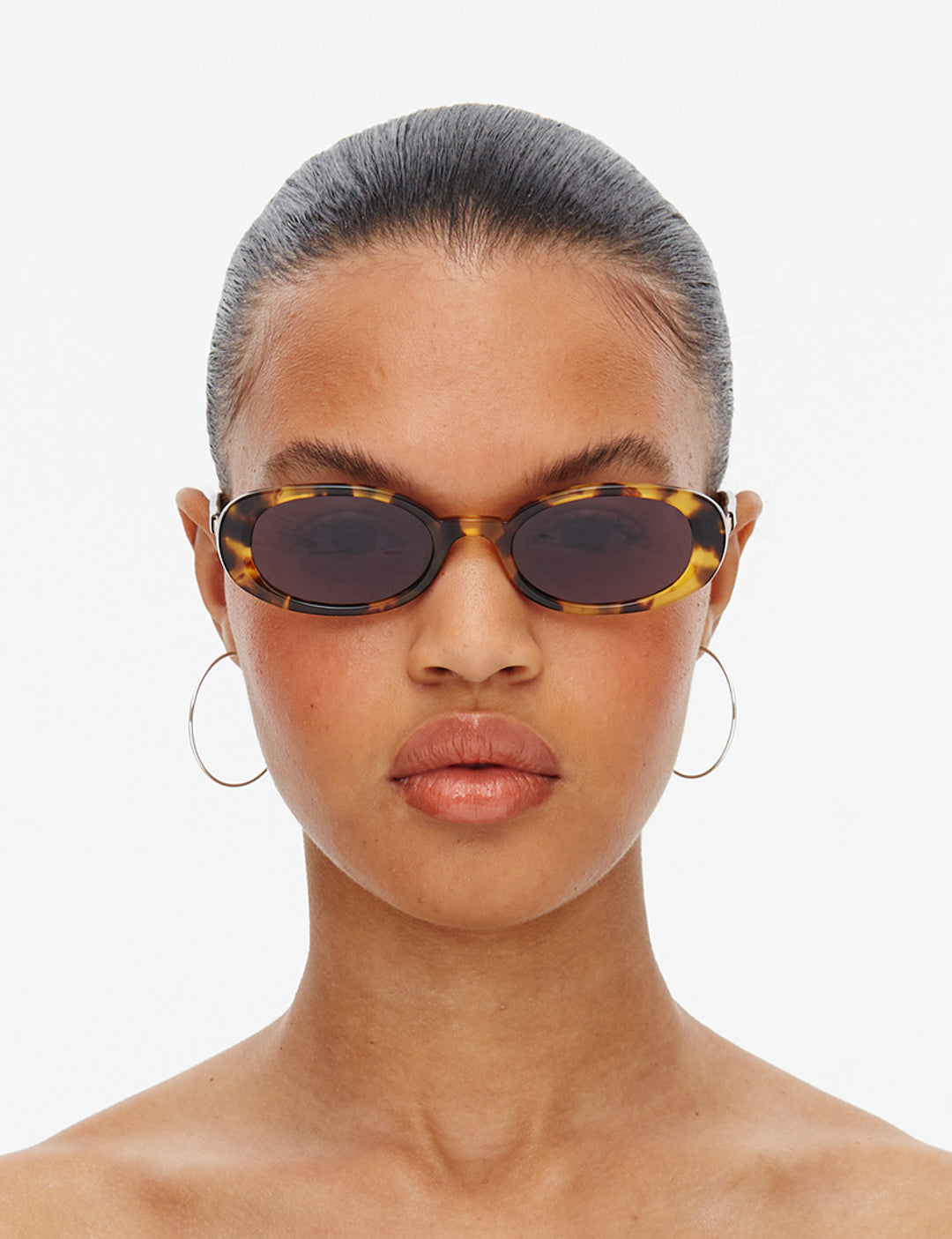 A pair of oval-shaped sunglasses with a tortoiseshell pattern frame and smoke-coloured lenses.