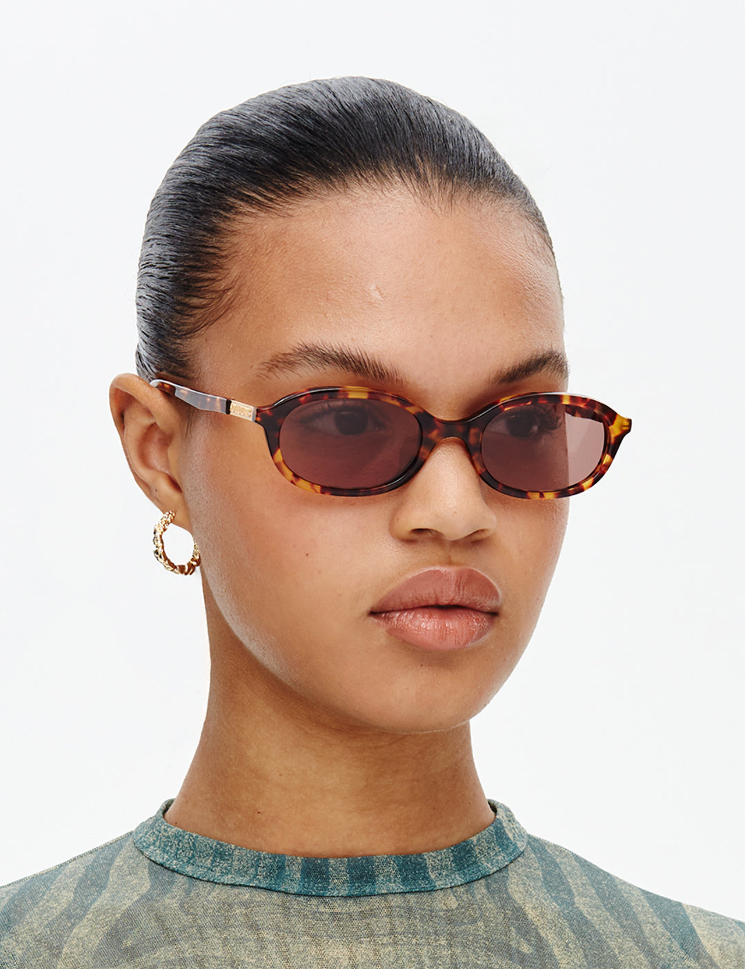 Person wearing tortoiseshell sunglasses with a neutral background