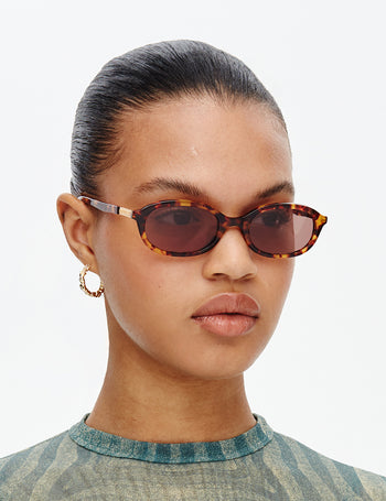 Person wearing tortoiseshell sunglasses with a neutral background